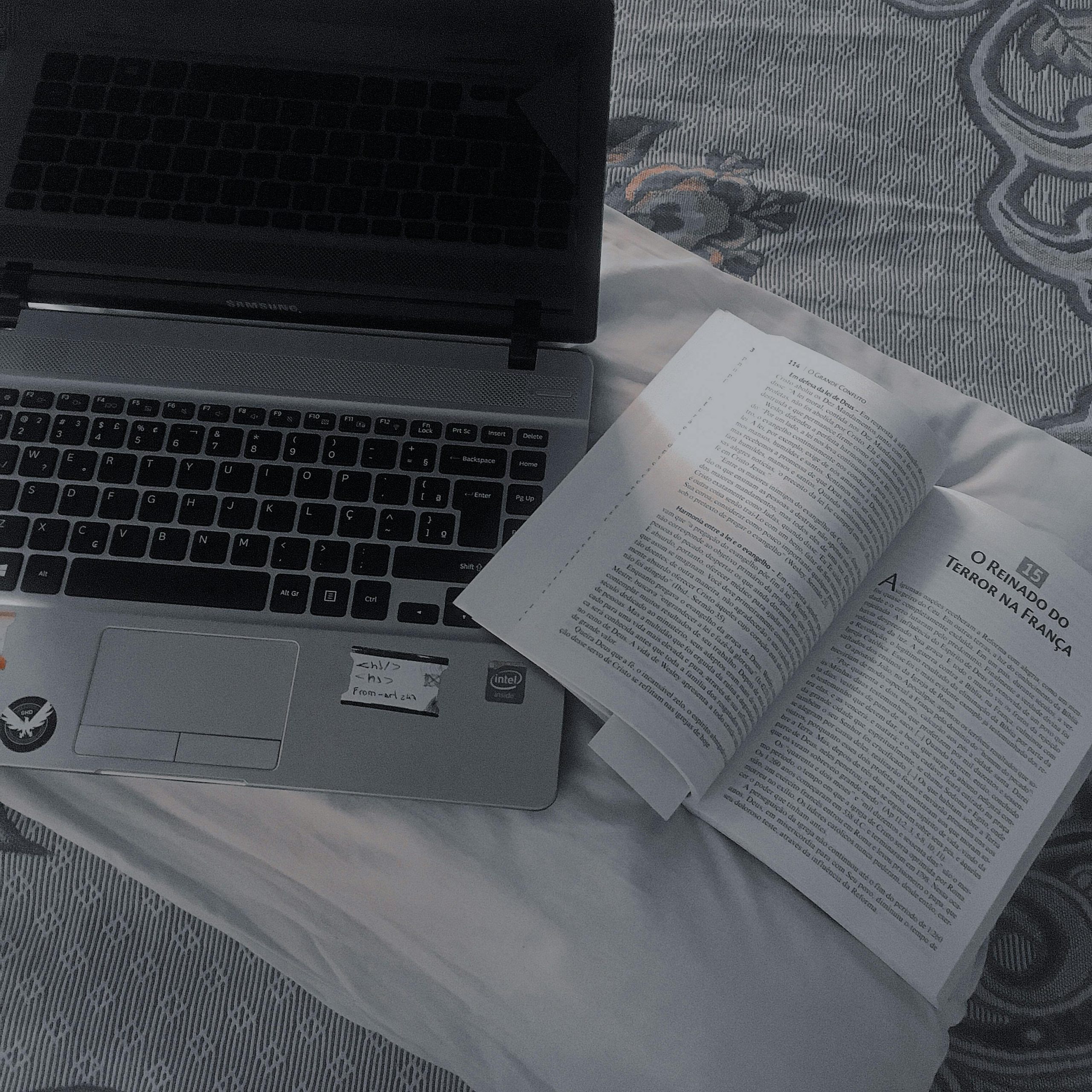 A cozy setup with an open book and laptop on a bedspread, perfect for study or work.